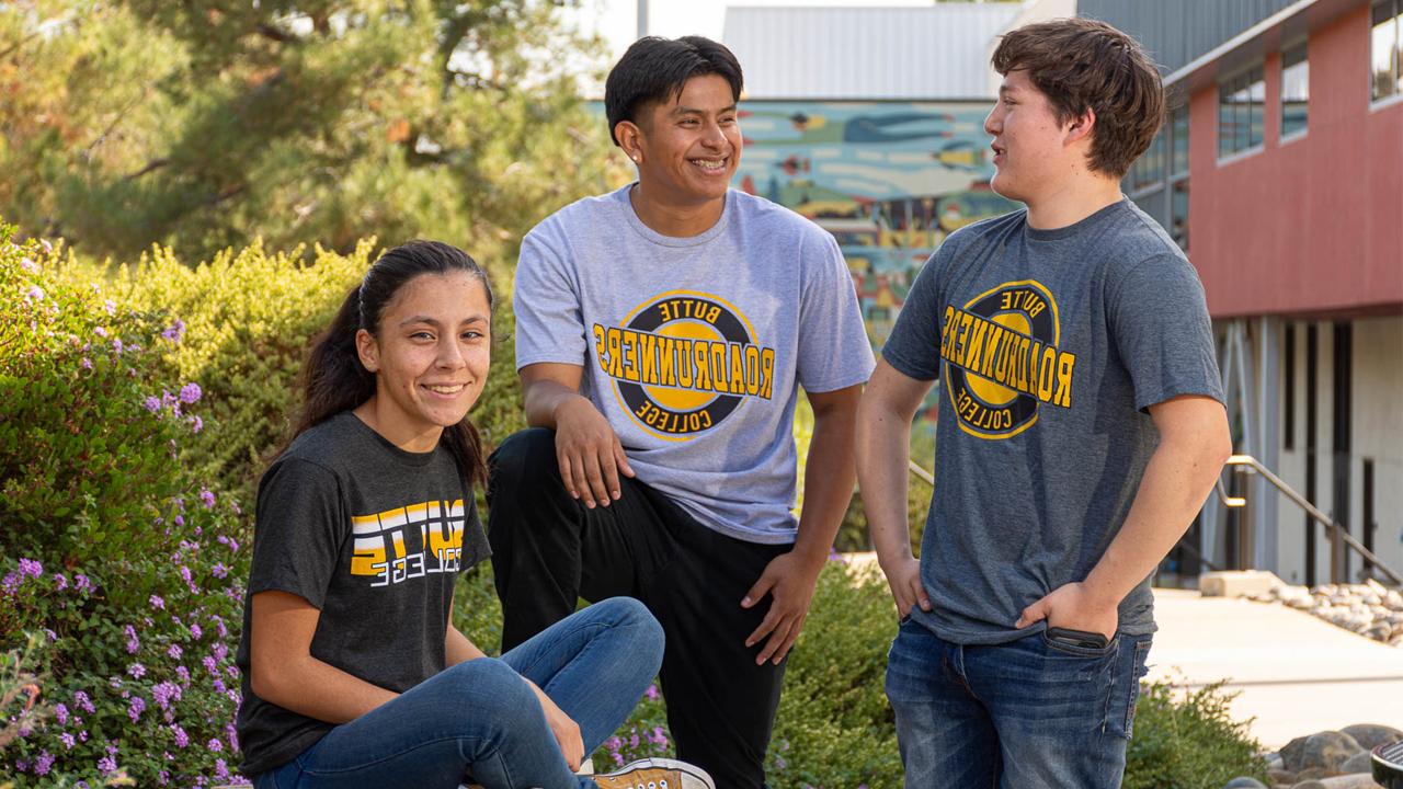 three students wearing Butte College shirts sit and chat outside of a campus building